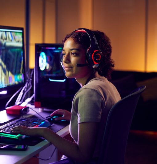 Teenage Girl Wearing Headset Gaming At Home Using Dual Computer Screens